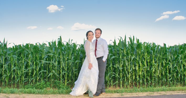 a bride and groom standing in front of a corn field