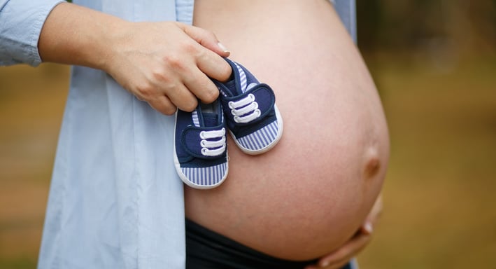 Mulher grávida segurando a barriga com sapatinhos azuis