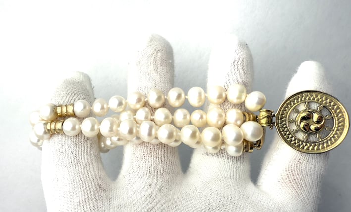 a woman's hand holding a bracelet with a gold coin