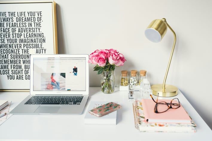 a laptop computer sitting on a desk with a vase of flowers