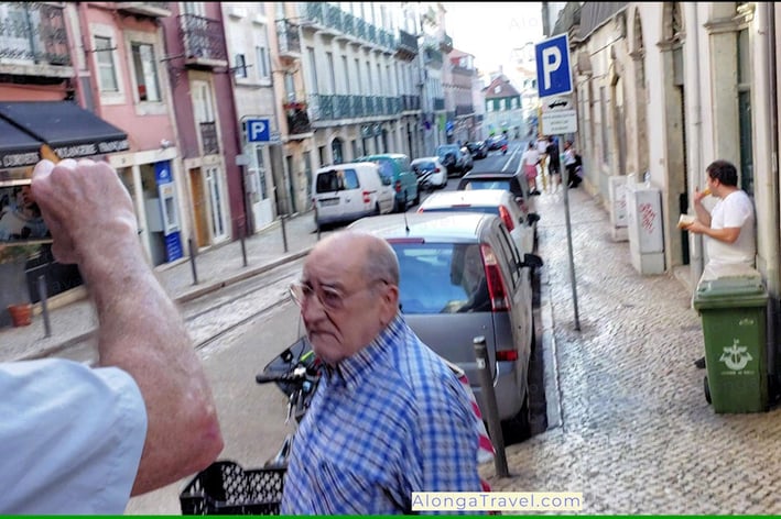 A guy extending an arm from a window of tram 28 to take a picture & almost hitting a guy on a street