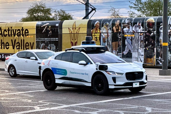 a white car driving down a street with a light rail train behind