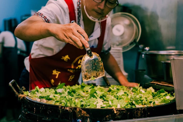 a man in a red apron making Taiwanese Oyster Omelette