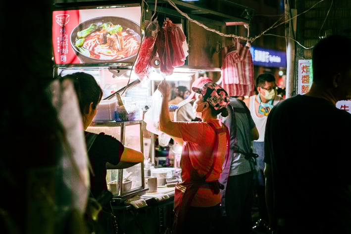 a woman is standing in front of a food vendor in Taiwan