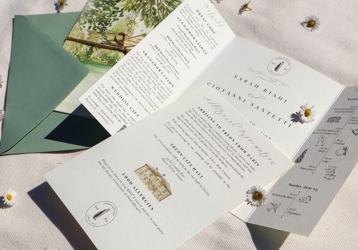 open wedding invitation with additional details card laid on top, closed invitation and envelope