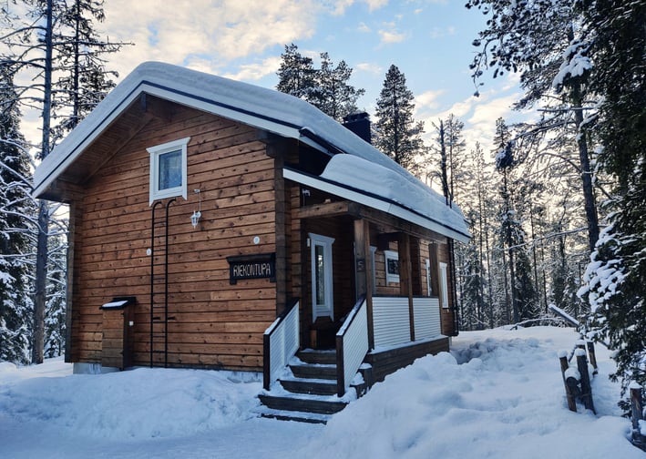 Snow covered log cabin set in lapland surrounded by forrests on a clear day