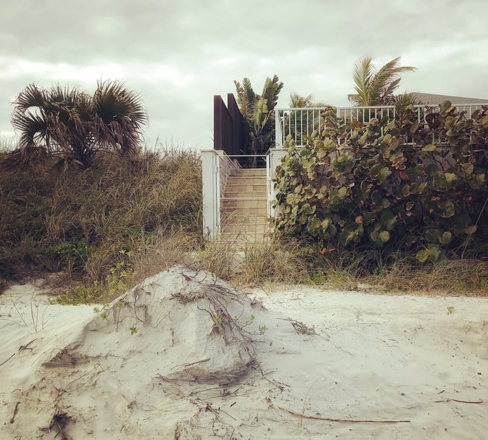 A moody photograph of an entrance to a house on a beach which shows the landscape around it.