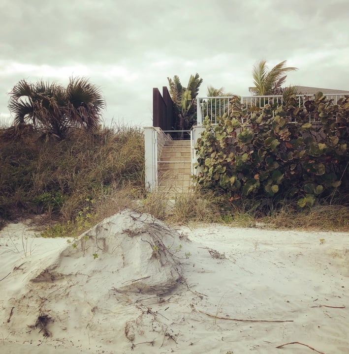 A moody photograph of an entrance to a house on a beach which shows the landscape around it.
