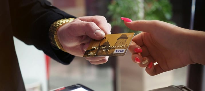 Person handing a gold Visa credit card to another person for payment at a terminal.