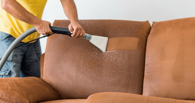 a man cleaning a couch with a vacuum cleaner