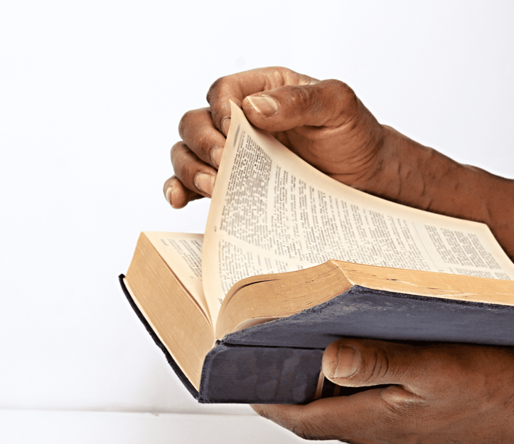 A pair of hands holding and flipping through the pages of an old, well-worn book, possibly a Bible.