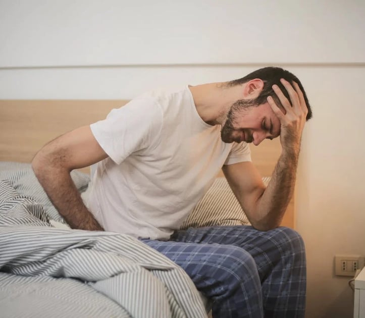 a man with a beard and glasses sitting on a bed