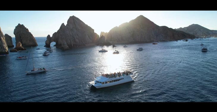A drone's aerial perspective captures a boat gathering near the iconic Cabo San Lucas arch. Highlighting videography service