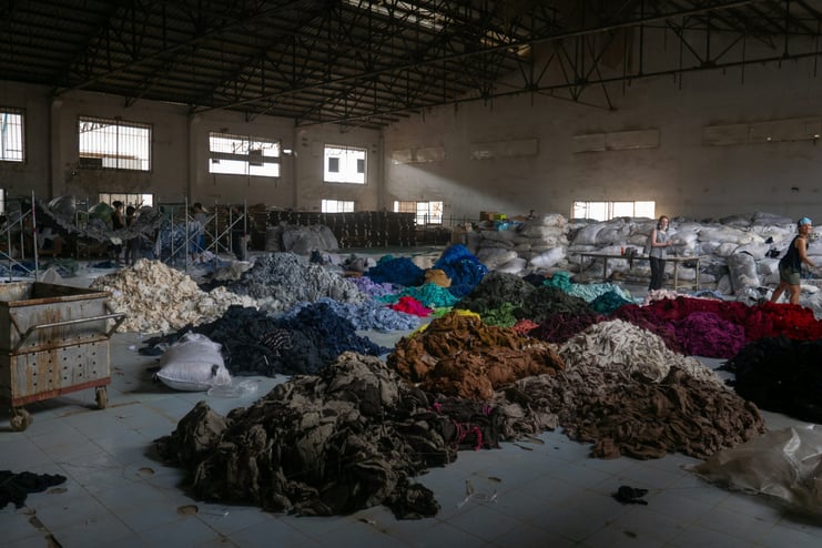 Multiple large color-coded piles of fabric in a warehouse