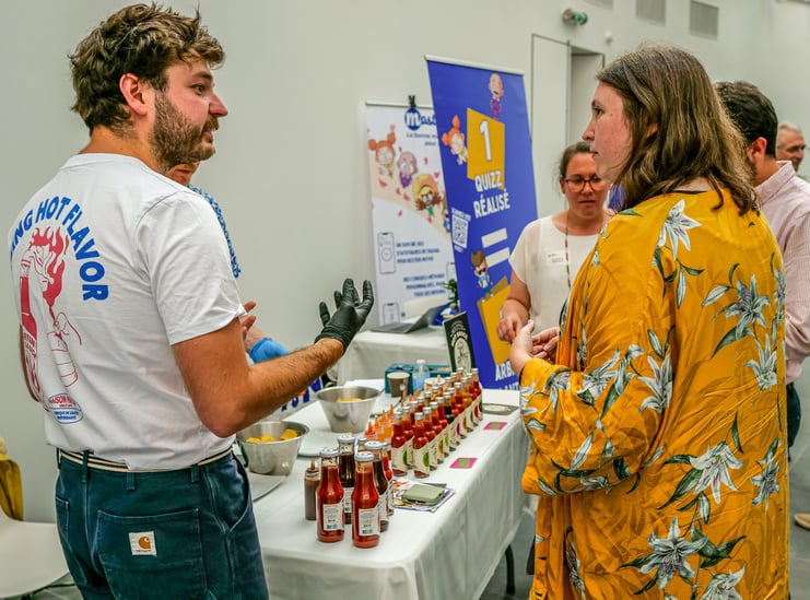 Groupe de personnes qui discutent autour d'un stand qui vend des sauces pimentées