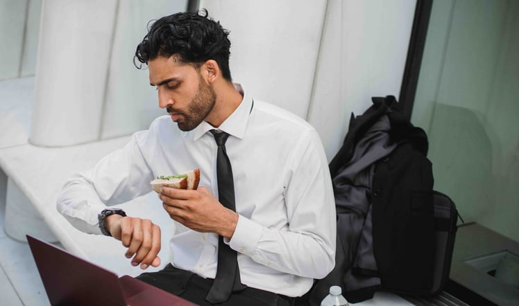 a man at office eating sandwich while looking at time