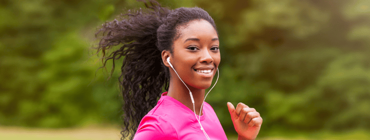Une jeune femme noire aux cheveux naturels et un haut de sport rose qui fait son jogging