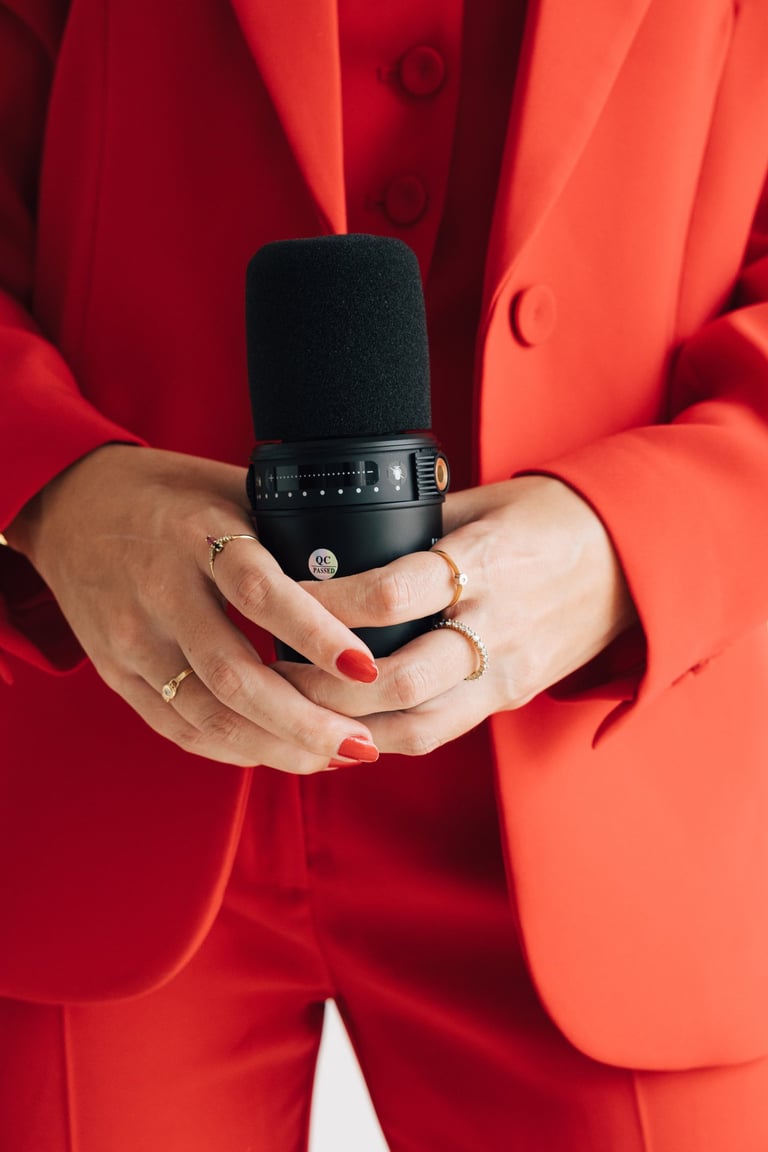 Primer plano de manos sujetando un micrófono de podcast con traje rojo.