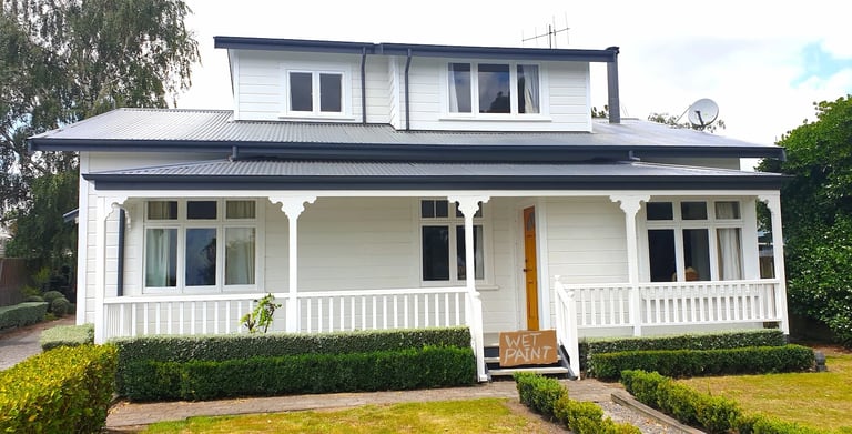 White weatherboard home with dark roof and porch detailing, freshly painted by Glen Currie of Gee Cee Painter