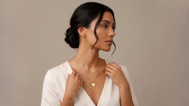 Elegant woman wearing a layered gold necklace with a round coin pendant and a white linen top.
