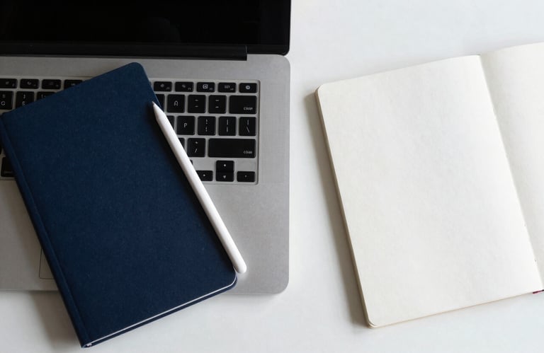 A top-down view of a minimalist desk setup featuring a sleek laptop, a digital stylus, and a notebook in shades of deep midnight blue and bright frost white.