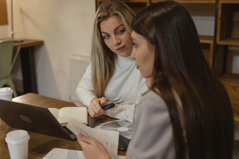 Two female students discussing and reviewing educational materials on a laptop computer.