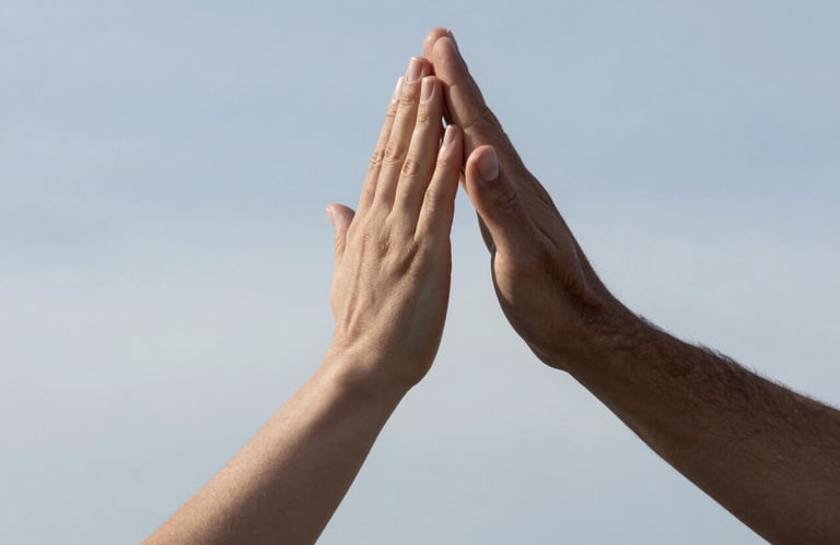 A close-up of two people's hands giving a high-five in a brightly lit, professional setting with mist and sky blue background tones.