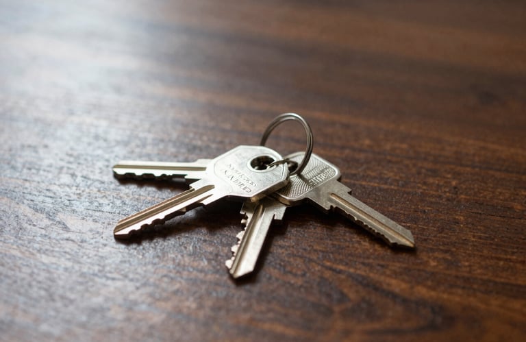 A professional photography shot of a set of silver house keys resting on a polished dark wood table with soft sunlight streaming in, North American / US style.