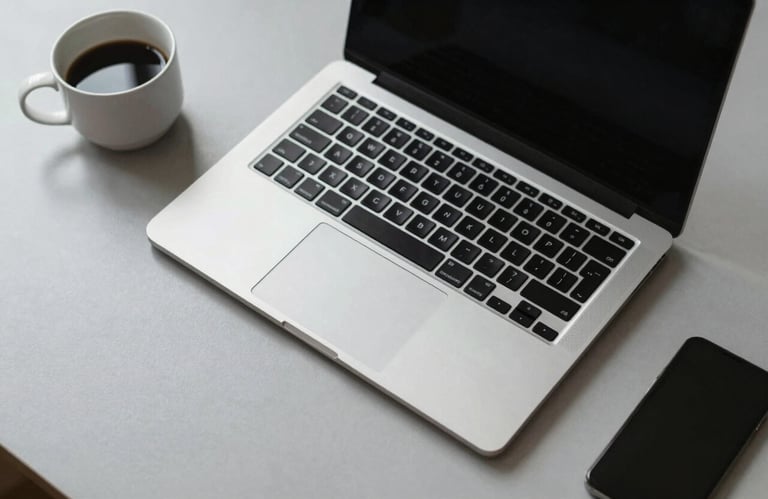 A high-angle shot of a minimalist workstation with a sleek laptop and a cup of coffee on a light grey surface, representing clean design and focus. North American setting.