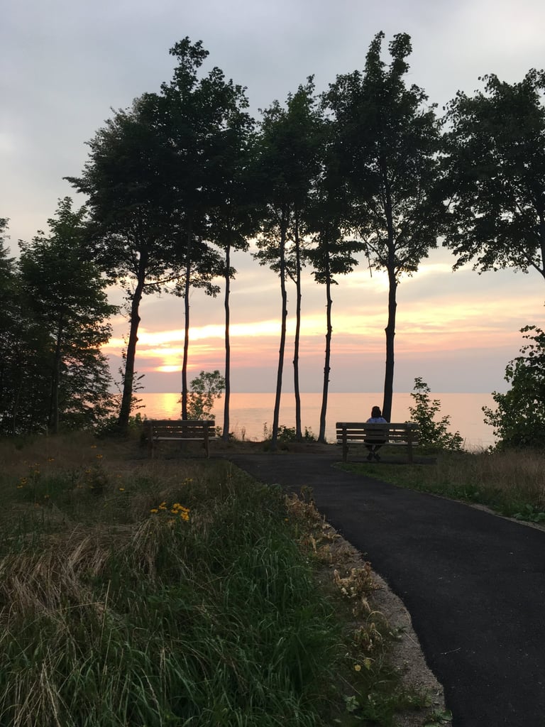 A woman sitting at a bench overlooking a lake at sunset.
