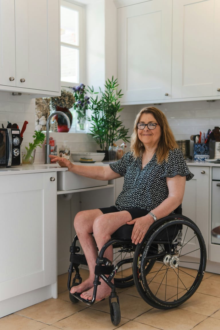 A smiling woman in a wheelchair using an accessible white modern kitchen with low counters.