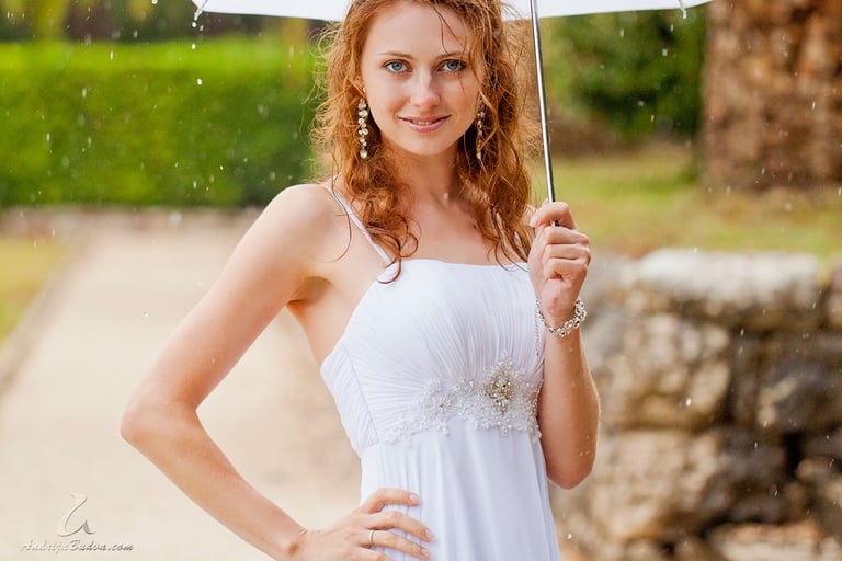 Photo of the bride in the wedding dress holding umbrella under the rain