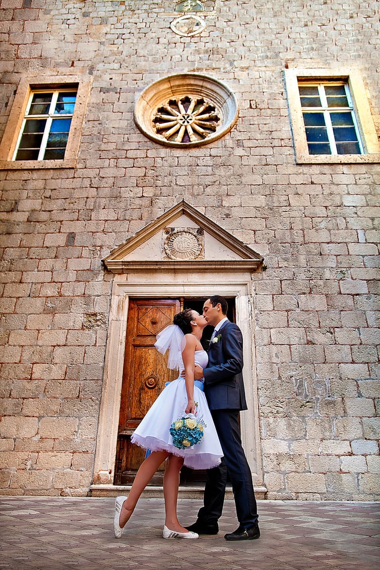 Bride and groom kissing in front of the old church in the old town of Kotor