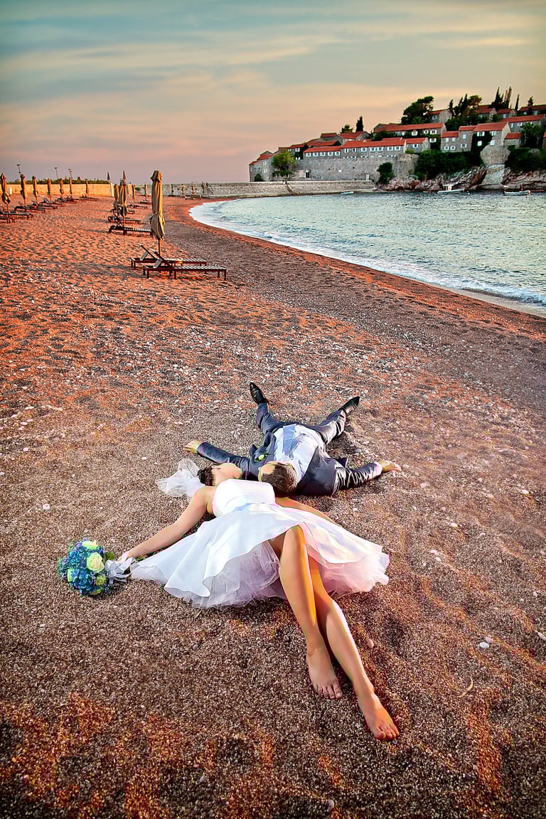 Bride and groom laying on the sandy beach of Sveti Stefan, Budva