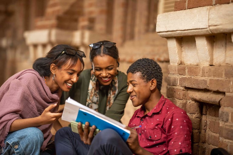 Close-up of three smiling Sudanese students discussing notes together.