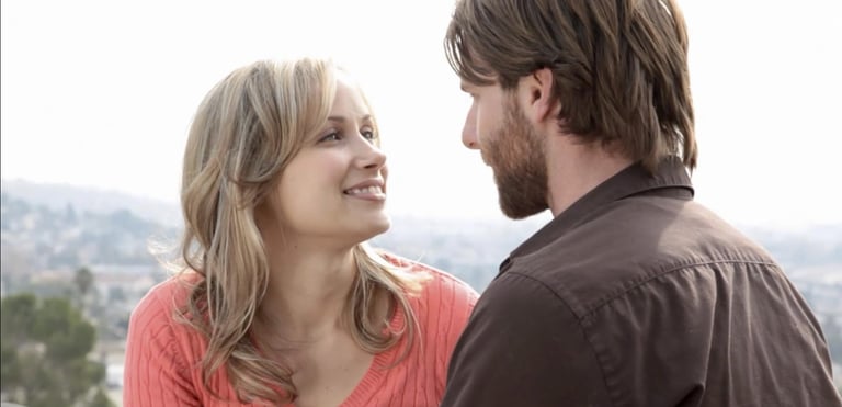 A thirty-something man and woman sit on a balcony looking into each other's eyes
