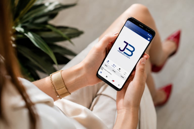 Woman holding a smartphone displaying the JB Inmobiliaria real estate agency logo on screen.