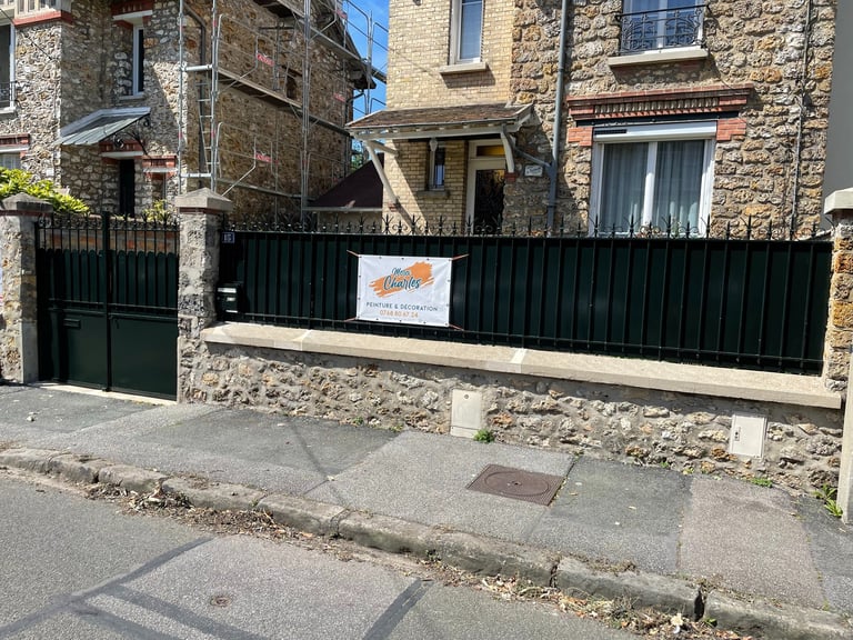 Stone house front with scaffolding and a black iron fence featuring a painting contractor sign.