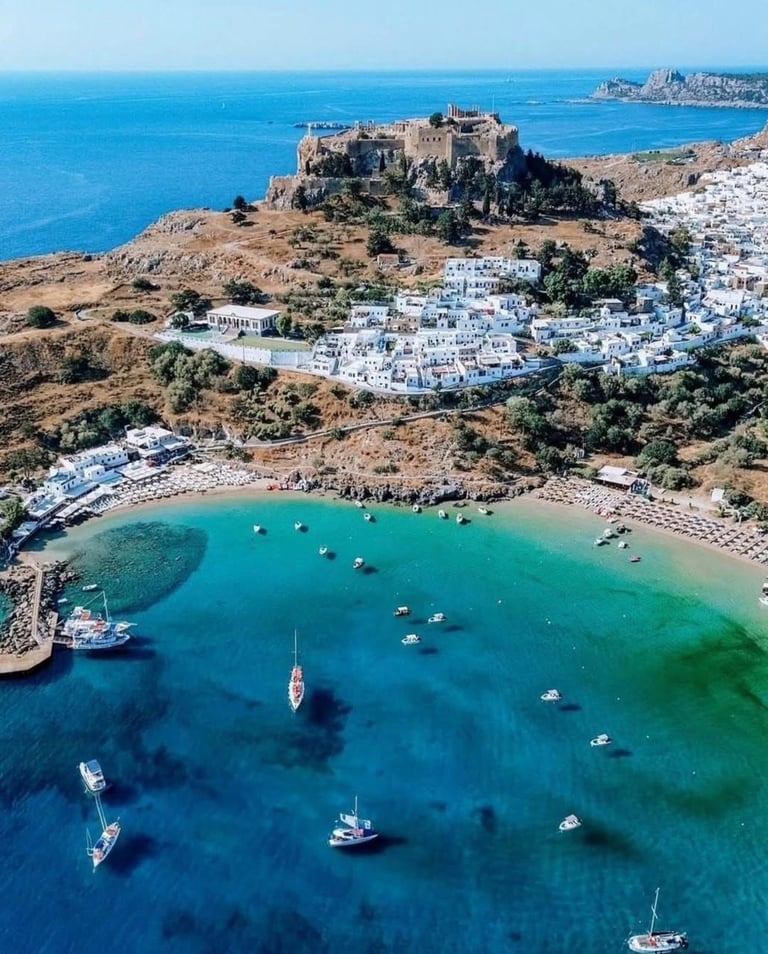 Aerial view of Lindos village and Acropolis with turquoise bay in Rhodes, Greece.