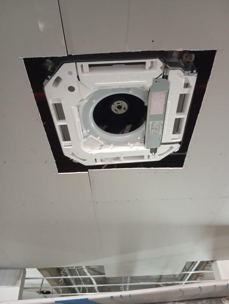 A ceiling-mounted cassette air conditioning unit being installed into a drop ceiling panel.