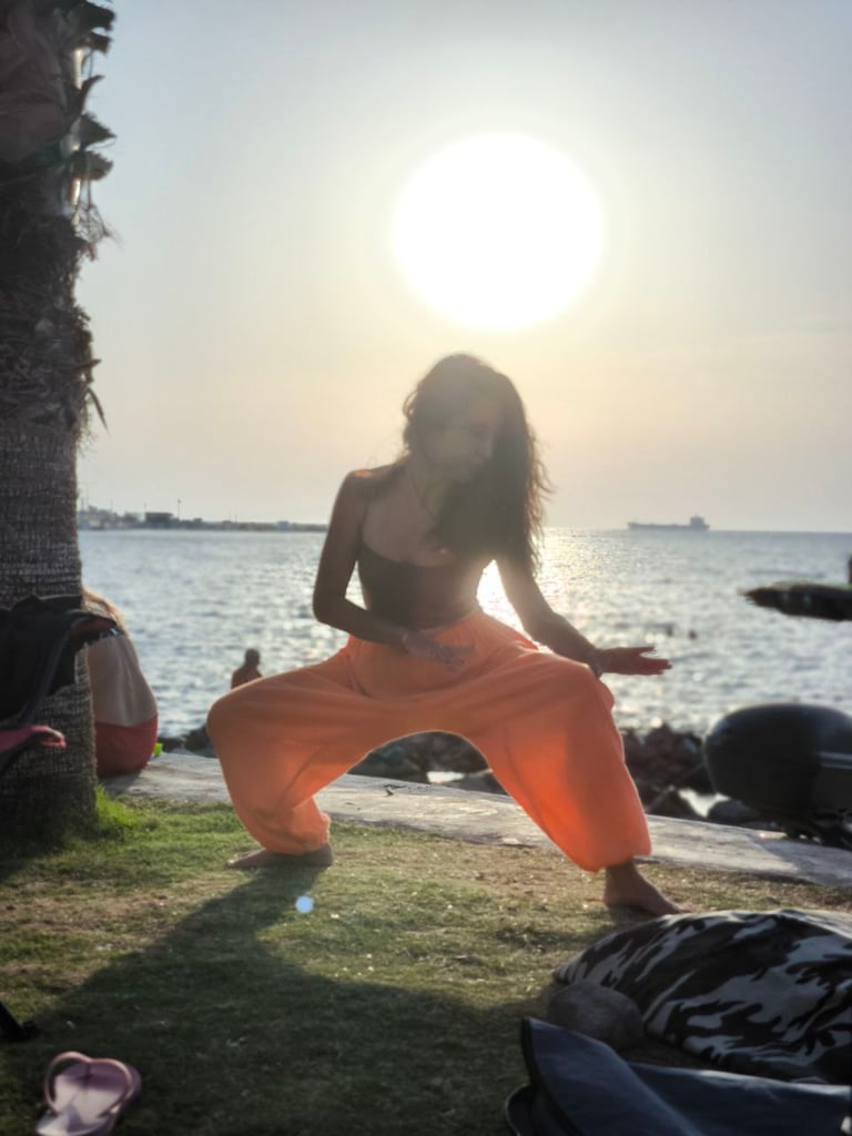 Gizem Kara practicing Tai Ji at sunset by the sea, in taming tiger stance, glowing in backlight.