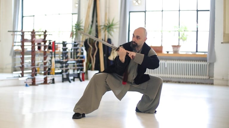 Ismet Himmet practicing a Wudang Jian sword form indoors, in a deep stance near weapon racks.