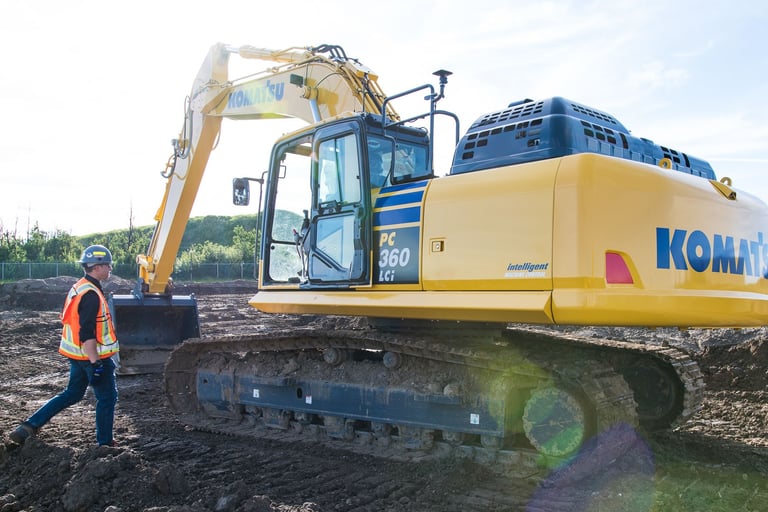A heavy equipment technician is seen approaching a Komatsu PC360LCi smart construction excavator.