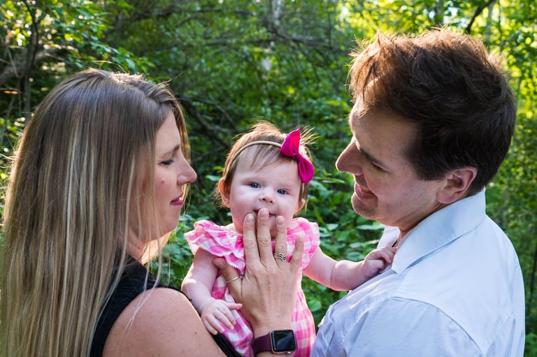 A happy couple holding the child and gazing at her. The child glances at the camera, smiling slightly. 