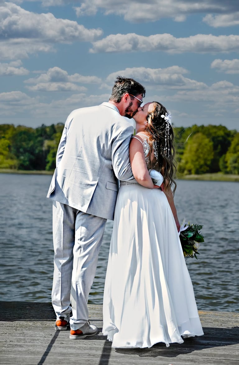 Romantisches Hochzeitsfoto am Möhnesee – Braut und Bräutigam küssen sich auf einem Steg am Wasser.“