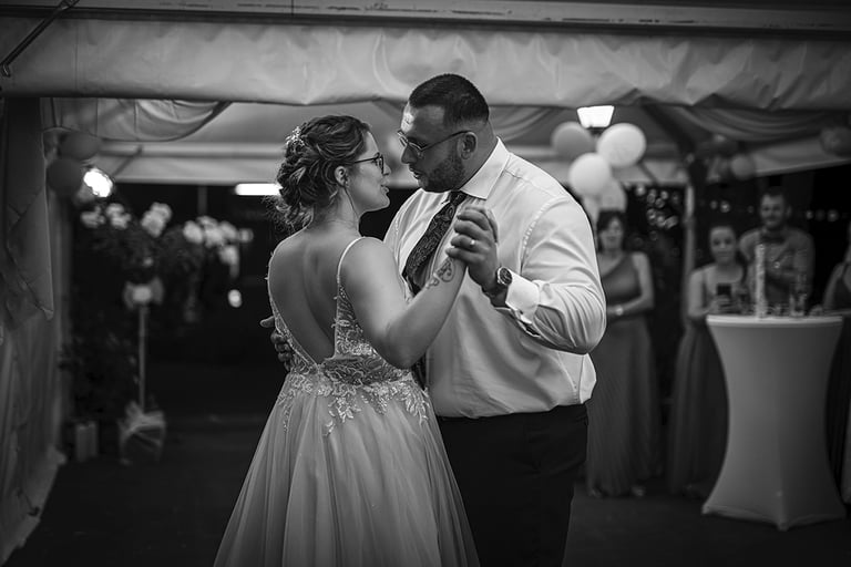 Ein Schwarz-Weiß-Foto eines Brautpaares, das bei seiner Hochzeit tanzt, wobei die Braut ein rückenfreies Kleid trägt und der 