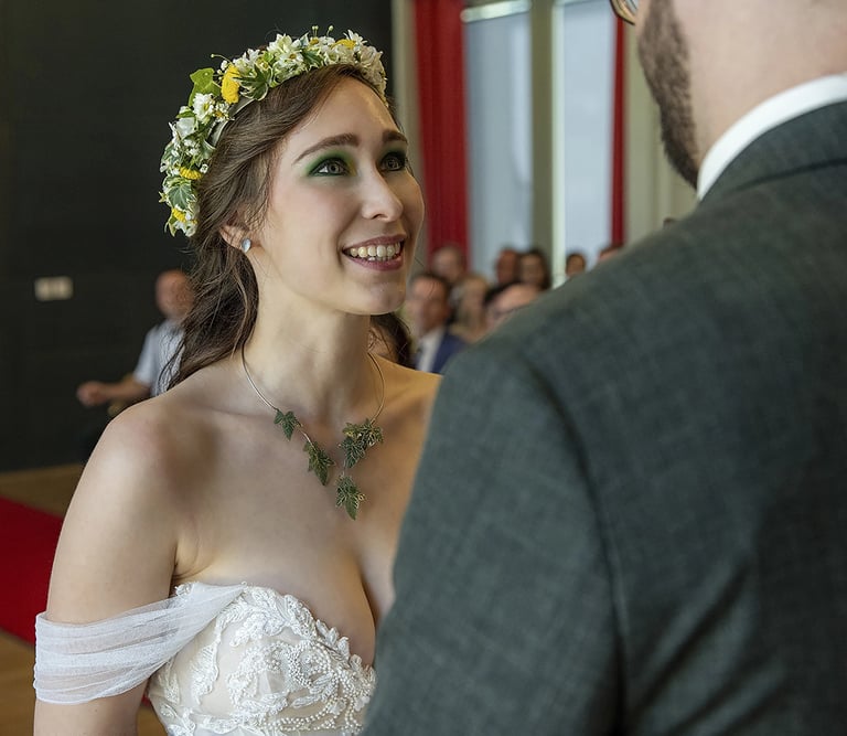 Ein Nahaufnahme-Foto einer lächelnden Braut, die nach oben zu ihrem Bräutigam blickt, dessen Rücken teilweise im Vordergrund 