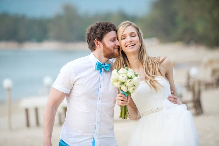 Groom kisses smiling bride holding white rose bouquet