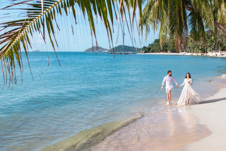 Wedding couple walking along Khem Beach under palm leaves