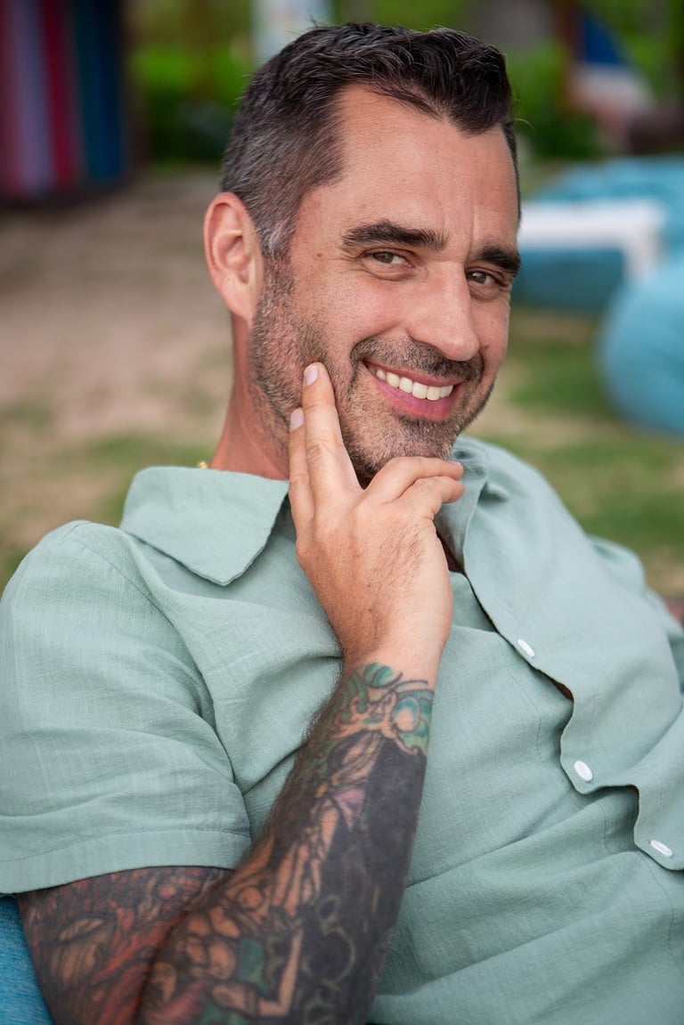 Relaxed solo portrait with tattooed arm and warm smile in beach bar